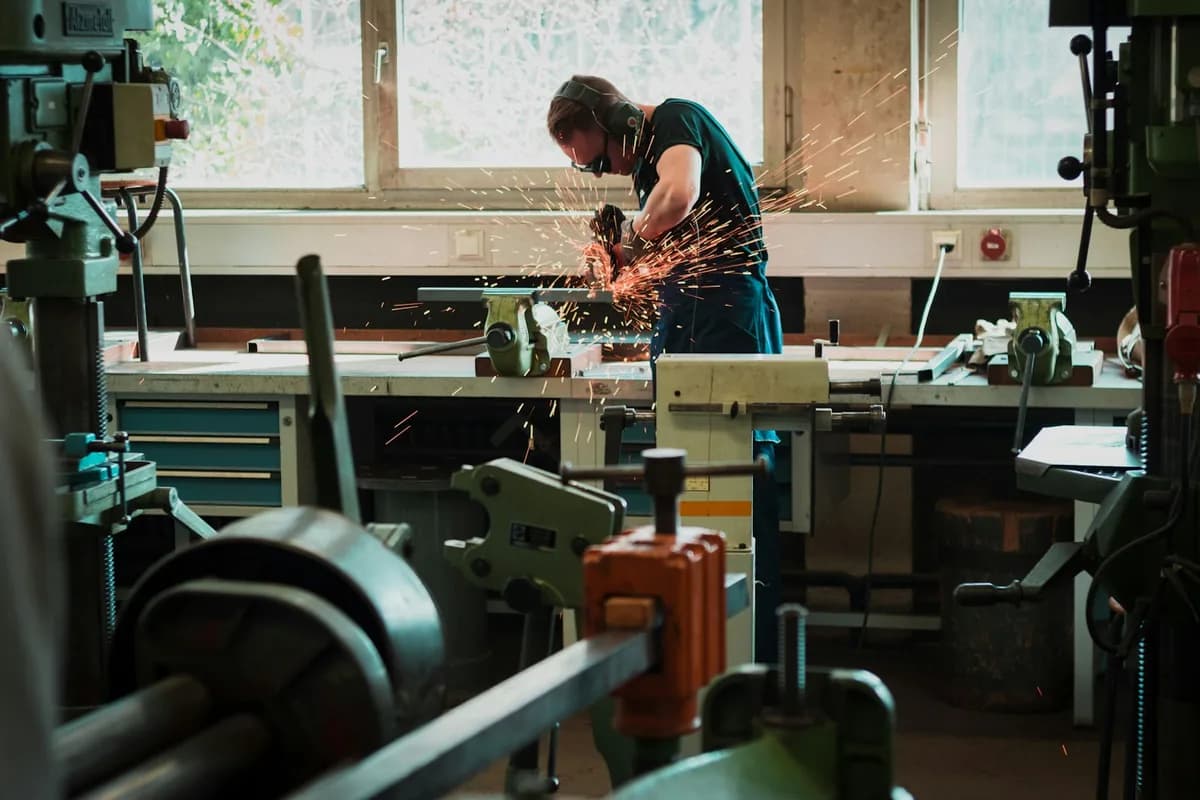 A maker cutting metal at a workshop bench, sparks flying