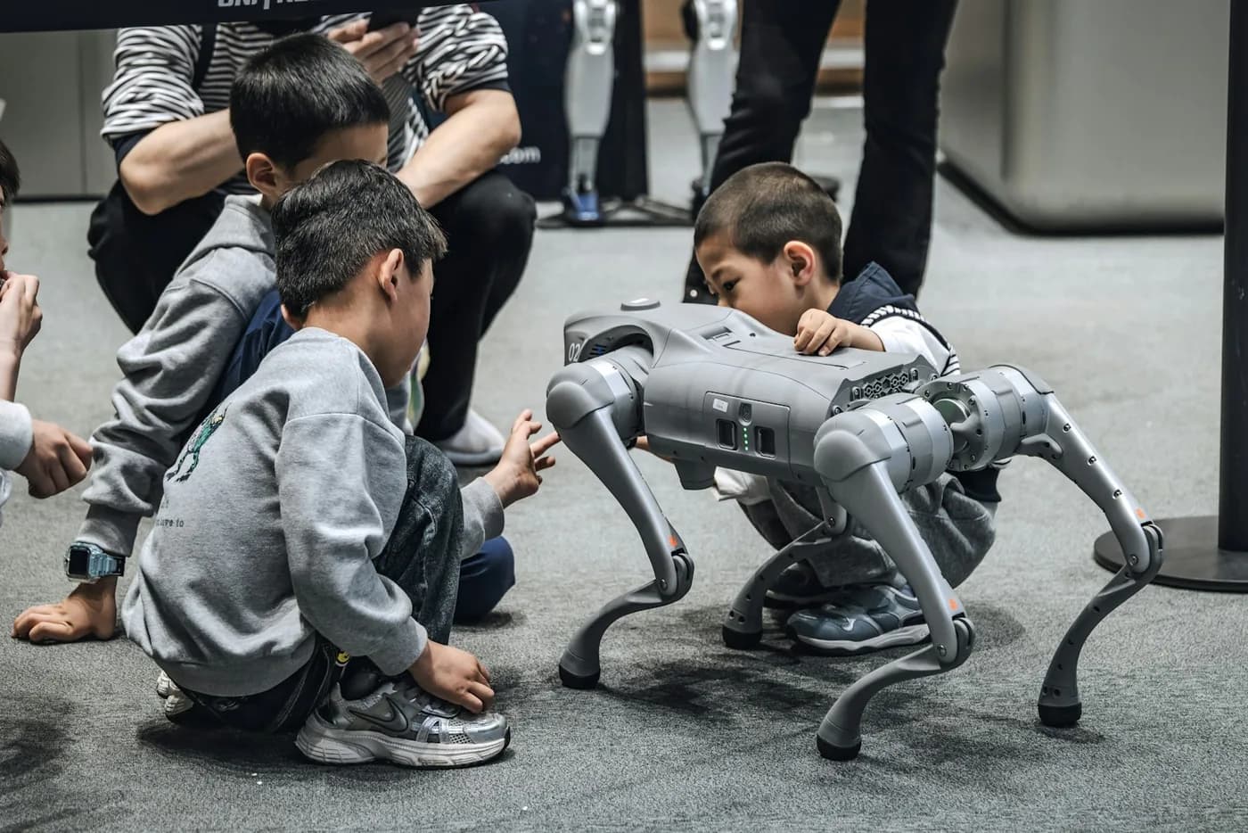 Children crouching to inspect a four-legged walking robot